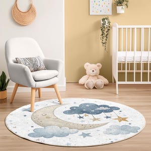Pode incluir: Tapete redondo para berçário com uma lua crescente sorridente, nuvens azuis e estrelas douradas penduradas. O tapete tem um fundo branco com estrelas azuis e douradas espalhadas. O design é adequado para um quarto de bebê.