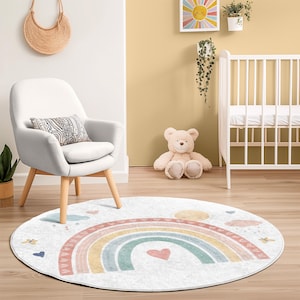 May include: A white round rug with a rainbow design and a pink heart in the center. The rainbow has yellow, orange, green, and blue stripes. There are also small pink hearts, clouds, and butterflies on the rug.