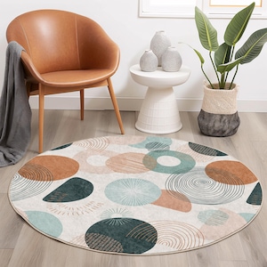 Può includere: Un tappeto rotondo color crema con un motivo geometrico di cerchi sovrapposti in tonalità di marrone, verde e blu. Il tappeto ha una superficie leggermente strutturata.