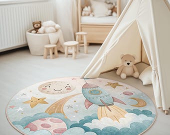 Puede incluir: Una alfombra redonda azul y blanca con un cohete, estrellas y una luna con una cara sonriente. La alfombra es perfecta para la habitación de un niño.