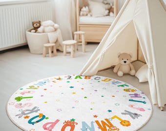 May include: A white round play mat with a colorful alphabet border and stars. The mat is on a white floor in a room with a white teepee tent and a wooden toy shelf.