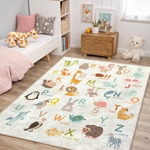 Peut inclure: Un tapis rectangulaire blanc cassé pour enfants avec un motif d'alphabet et des illustrations d'animaux colorés. Chaque lettre a un animal correspondant, comme une girafe pour 'G' et un zèbre pour 'Z'. Le tapis est posé sur un sol en bois.