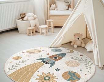 Puede incluir: Una alfombra de juego redonda de color crema con un cohete, planetas, estrellas y flores. La alfombra está sobre un suelo de madera clara en una habitación con una tienda de campaña tipi.
