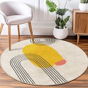 May include: A round, cream-colored rug with a modern abstract design. The design features black lines forming a curved shape, a yellow circle, and a small pink circle.