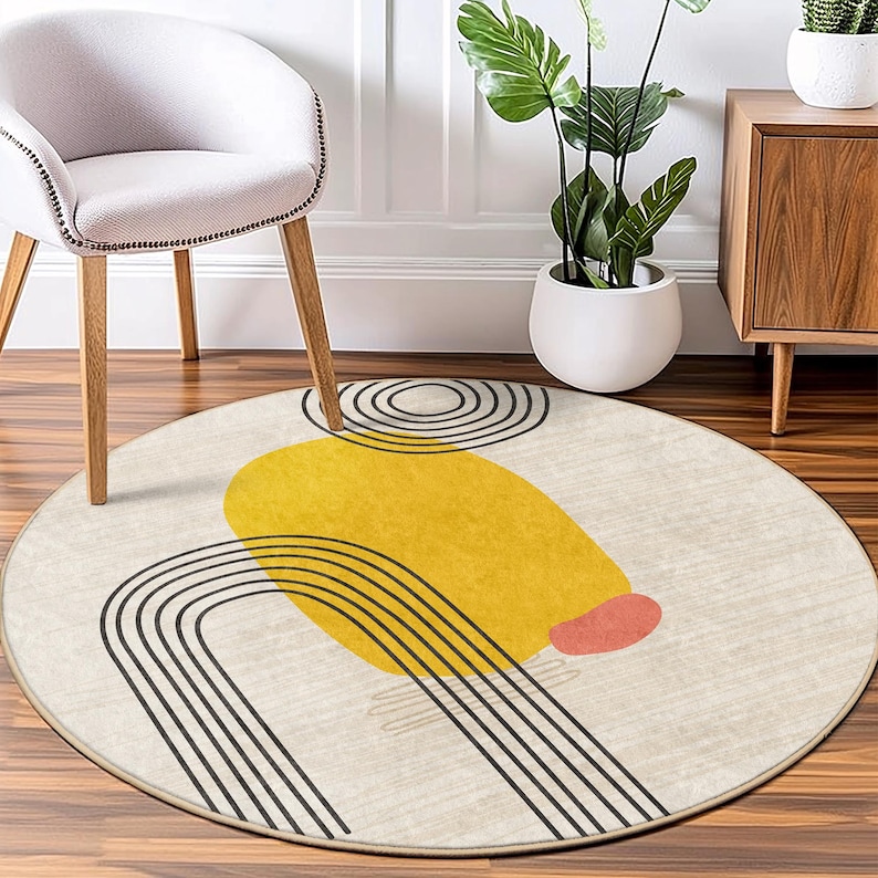 May include: A round, cream-colored rug with a modern abstract design. The design features black lines forming a curved shape, a yellow circle, and a small pink circle.