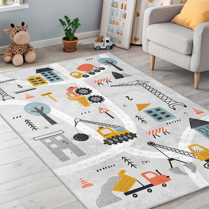 May include: A grey children's rug with a construction theme. The rug features roads, buildings, trees, and construction vehicles in yellow, orange, and blue. The design includes a dump truck, crane, and bulldozer.