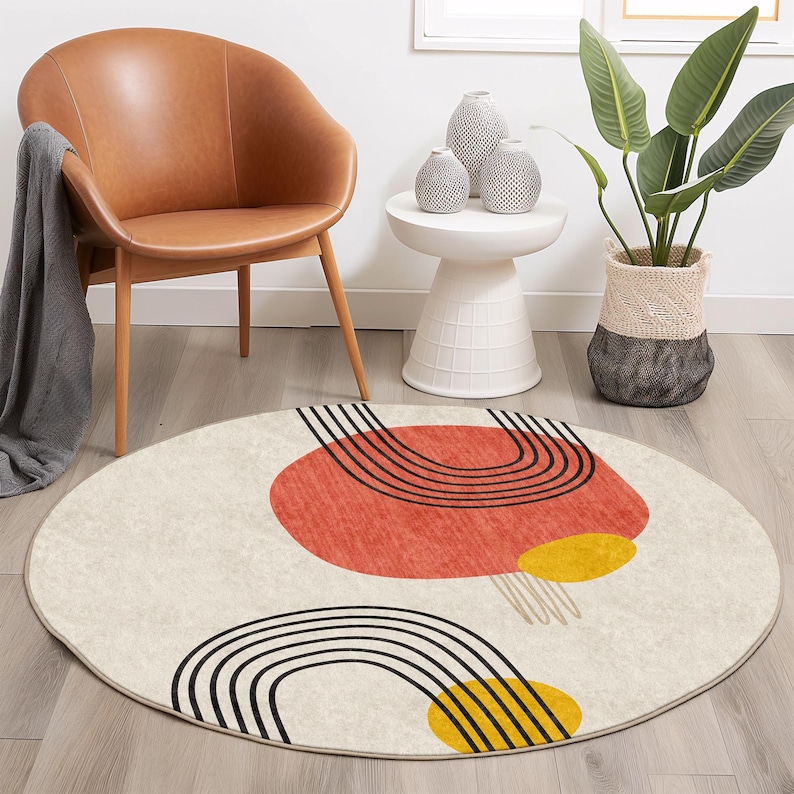 May include: A round, cream-colored rug with a geometric design featuring black, red, and yellow shapes. The rug has a subtle texture and a fringe border.