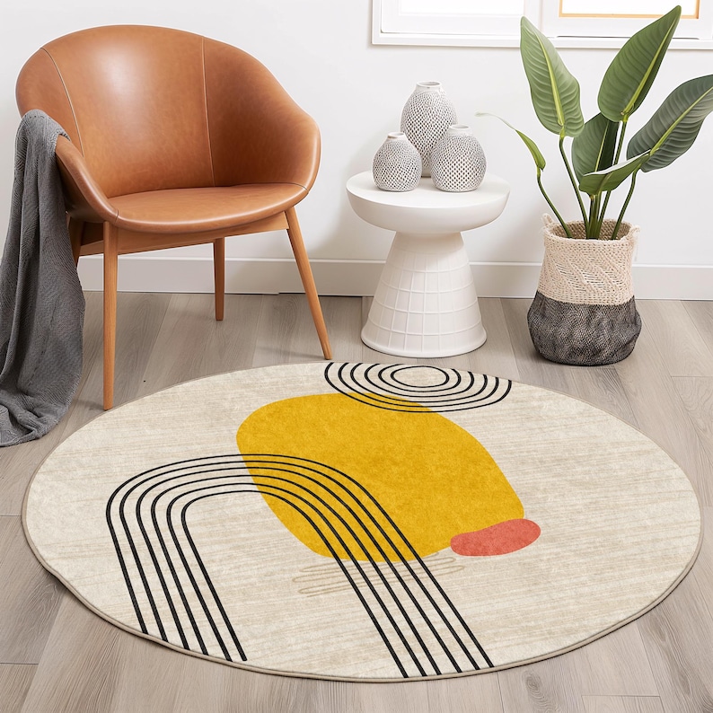 May include: A round, cream-colored rug with a black and yellow abstract design. The design features a large yellow circle with black stripes and a smaller red circle.
