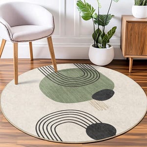May include: A round, cream-colored rug with a geometric design featuring black lines and green and black circles. The rug has a subtle texture and a fringe border.