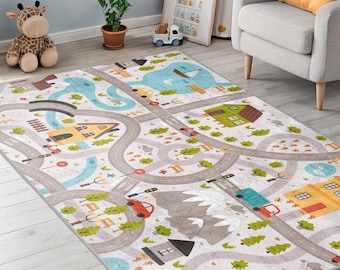 Puede incluir: Una alfombra de juego rectangular con un diseño de mapa de carreteras. Presenta carreteras grises sinuosas, casas coloridas, árboles y vehículos. La alfombra tiene un fondo gris claro con acentos azules y verdes, creando una escena lúdica.