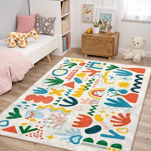 May include: A rectangular area rug with a cream background and a colorful abstract design. The design includes shapes in red, yellow, blue, green, and orange. The rug is placed in a child's bedroom.