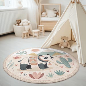 Op de afbeelding: Een rond, crèmekleurig tapijt met een speels ontwerp met een panda die een kleurrijk patroon trui draagt, cactussen en bloemen. Het tapijt is perfect voor een kinderkamer of slaapkamer.