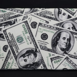 May include: A white fabric wallet with a pattern of repeated images of US $100 bills. The bills feature Benjamin Franklin's portrait and the text "UNITED STATES OF AMERICA" and "ONE HUNDRED DOLLARS".