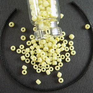 May include: A glass jar filled with small, pale yellow glass beads. The beads are scattered on a black surface.