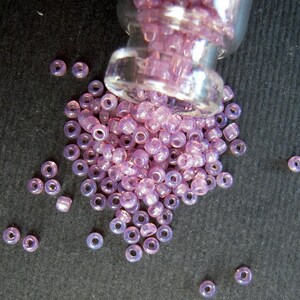 May include: A glass jar filled with small, iridescent purple beads. The beads are scattered on a dark gray surface.