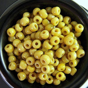 May include: A bowl filled with yellow glass beads. The beads are round and have a smooth, glossy finish.