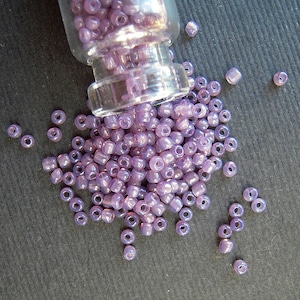 May include: A glass jar filled with small, iridescent purple beads. The jar is tipped over, spilling the beads onto a gray surface.