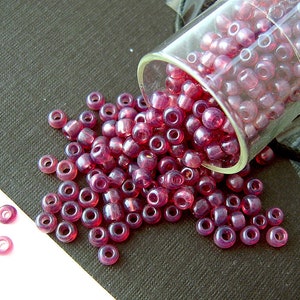 May include: A glass jar filled with small, translucent, pink beads. The beads are spilling out of the jar onto a dark surface.