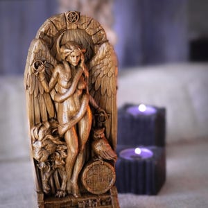 Könnte beinhalten: Eine braune, holzfarbene Reliefskulptur mit einer zentralen geflügelten Figur, die von einer Schlange umwunden ist, flankiert von einem Löwen und einer Eule. Der Bogenrahmen zeigt ein Pentagramm oben und ein kreisförmiges Siegel an der Basis.