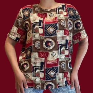 May include: Short-sleeved top with a geometric pattern in shades of brown, red, navy, and beige. The design features squares, circles, and diamond shapes. The top has a round neckline and short sleeves.
