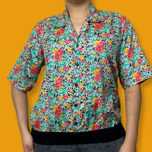 May include: A short-sleeved button-up shirt with a floral print in shades of red, yellow, green, and black. The shirt has a collar and a button-up front.