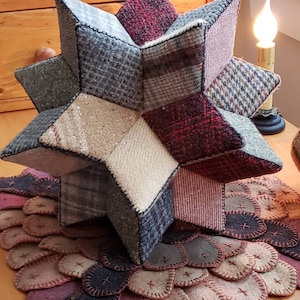 May include: A 3D star-shaped pillow made from patchwork fabric in shades of brown, gray, and red. The pillow is sitting on a circular rug made from smaller, overlapping fabric circles in shades of brown, gray, and red.