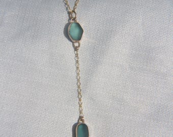 Puede incluir: Un collar de cadena en tono dorado con dos colgantes lisos estilo vidrio marino en tonos azul claro y verde azulado. El collar tiene un diseño en forma de Y con un colgante hexagonal sobre un segundo colgante ovalado más pequeño al final.