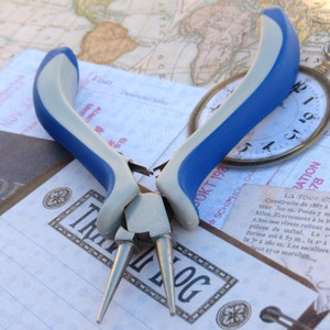 May include: Blue and silver jewelry pliers with a silver handle and two pointed tips. The pliers are on a white surface with text.