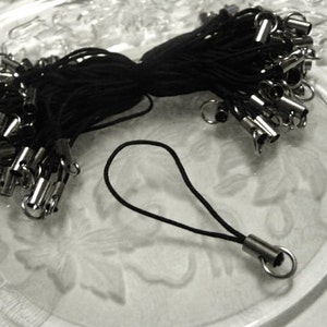May include: A bulk pack of black phone charms with silver metal tips. The charms are made of thin black string and have a loop at the end for attaching to a phone case.
