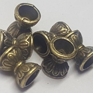 May include: Five antique gold-toned metal beads with a decorative floral design. The beads have a hollow center and a small opening on the side.