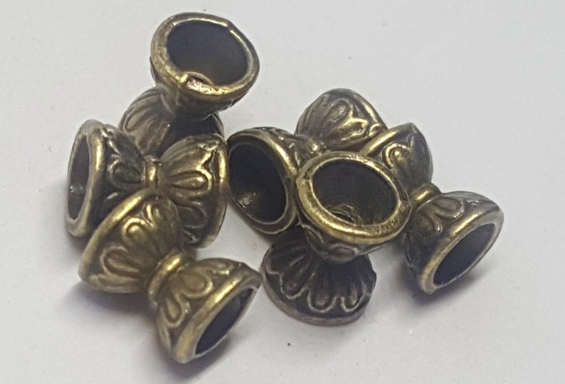 May include: Five antique gold-toned metal beads with a decorative floral design. The beads have a hollow center and a small opening on the side.