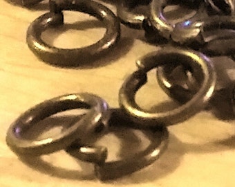 May include: A close-up of a pile of small, round, gold-colored metal jump rings. The rings are all the same size and are arranged in a random pattern.