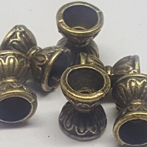 May include: Five antique gold-toned metal beads with intricate designs. Each bead has a round top and a round bottom with a raised design. The beads are perfect for jewelry making or other craft projects.