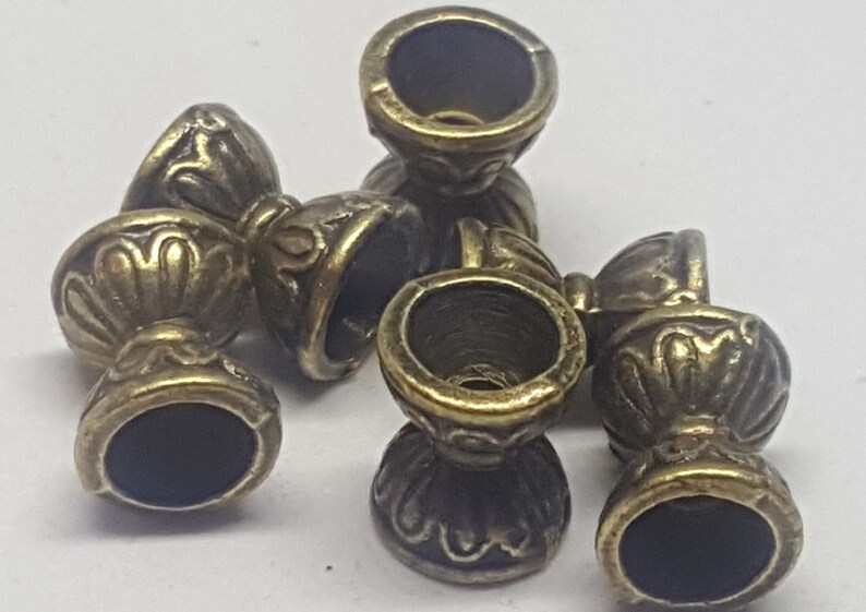 May include: Five antique gold-toned metal beads with intricate designs. Each bead has a round top and a round bottom with a raised design. The beads are perfect for jewelry making or other craft projects.