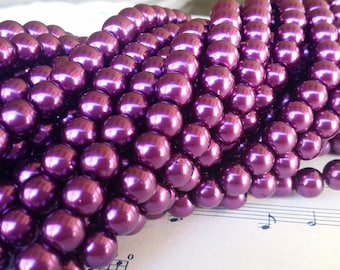 May include: A strand of deep purple faux pearl beads. The pearls are round and have a high gloss finish.