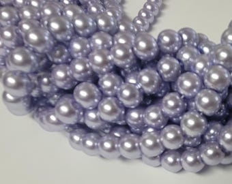 May include: Close-up of a collection of light purple faux pearls. The pearls are round and have a glossy finish, reflecting light. The pearls are clustered together, suggesting they are part of a necklace or other jewelry.