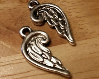 May include: Two silver angel wing charms with a detailed design. The wings are shaped like a heart and have a loop at the top for attaching to jewelry or other crafts.