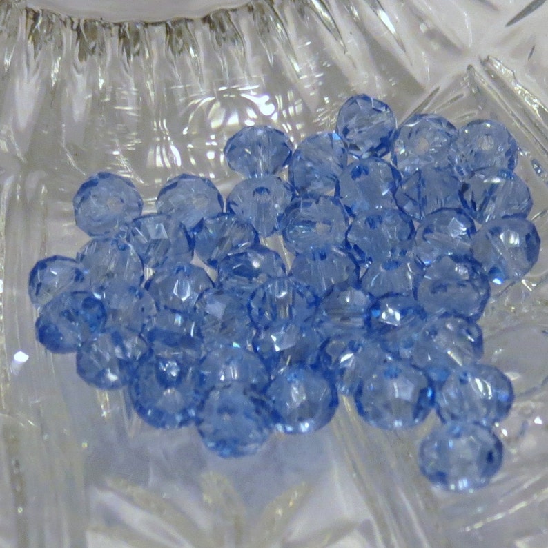 May include: A close-up of a pile of light blue crystal beads. The beads are faceted and have a shiny finish.