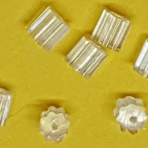 May include: A close-up of seven silver earring backs. The backs are small and square with a textured surface.
