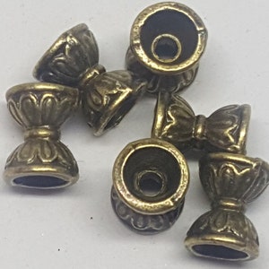May include: A set of six antique gold-toned metal beads with intricate floral designs. Each bead has a small hole in the center for stringing.