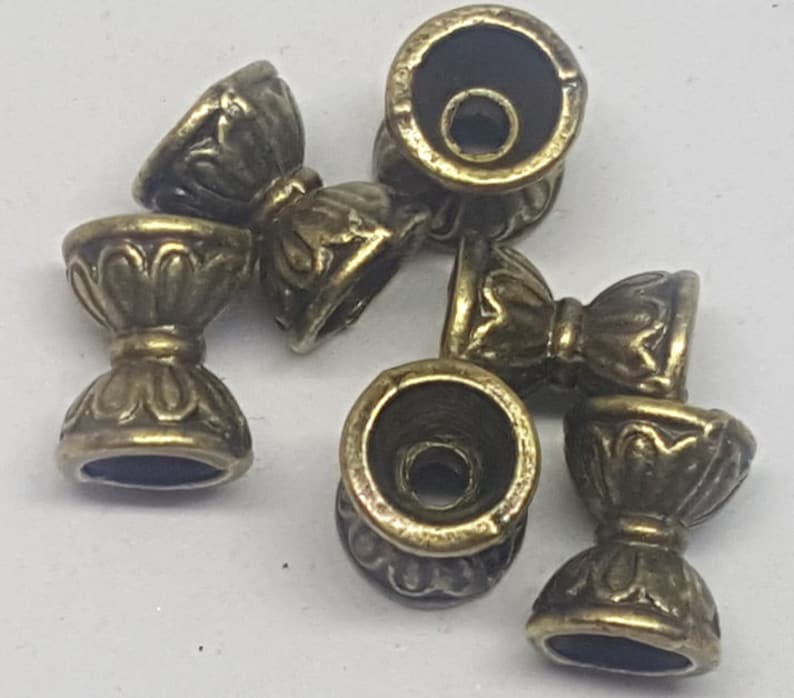 May include: A set of six antique gold-toned metal beads with intricate floral designs. Each bead has a small hole in the center for stringing.