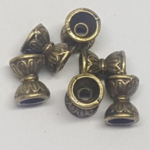 May include: Six antique gold-toned metal cup-shaped beads with intricate designs. The beads have a smooth, polished finish and are perfect for jewelry making or crafting.