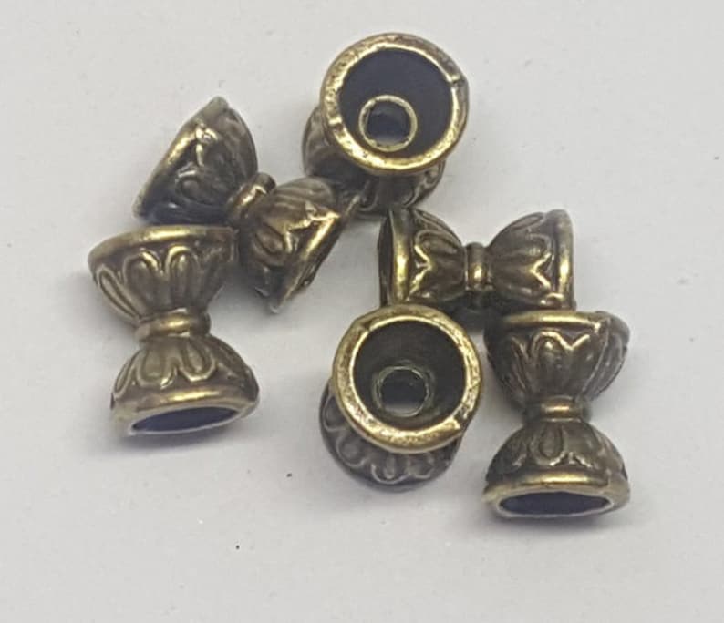 May include: Six antique gold-toned metal cup-shaped beads with intricate designs. The beads have a smooth, polished finish and are perfect for jewelry making or crafting.