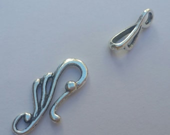 May include: Two silver metal clasps for jewelry making. One clasp is a simple loop, the other is a more ornate design with a swirl and a small ball.
