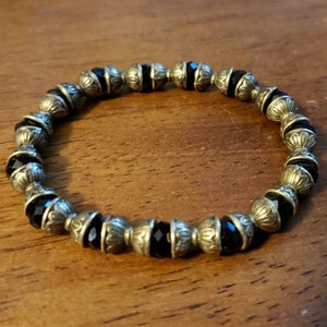 May include: A black and gold beaded bracelet with ornate metal accents. The bracelet is made of round black beads with gold metal accents.