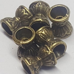 May include: A group of seven antique gold-toned metal bead caps with ornate designs. The caps have a round opening at the top and a decorative base.