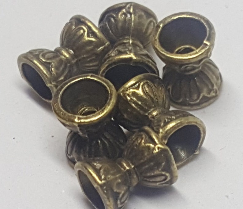 May include: A group of seven antique gold-toned metal bead caps with ornate designs. The caps have a round opening at the top and a decorative base.