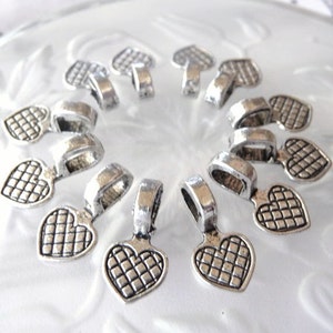 May include: A set of 12 silver-toned heart-shaped pendant charms with a textured design. Each charm has a loop at the top for attaching to jewelry or other crafts.