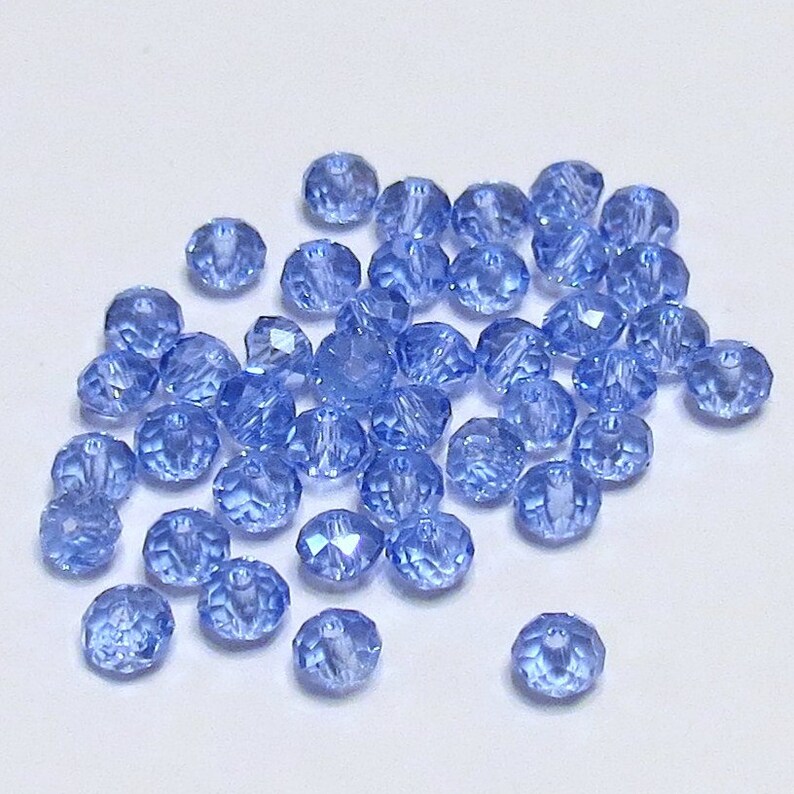 May include: A scattering of light blue glass beads, each with a faceted design. The beads are round and have a slight shimmer.
