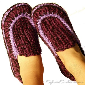 May include: Purple and black crocheted slippers with a purple trim. The slippers are worn on a person's feet.